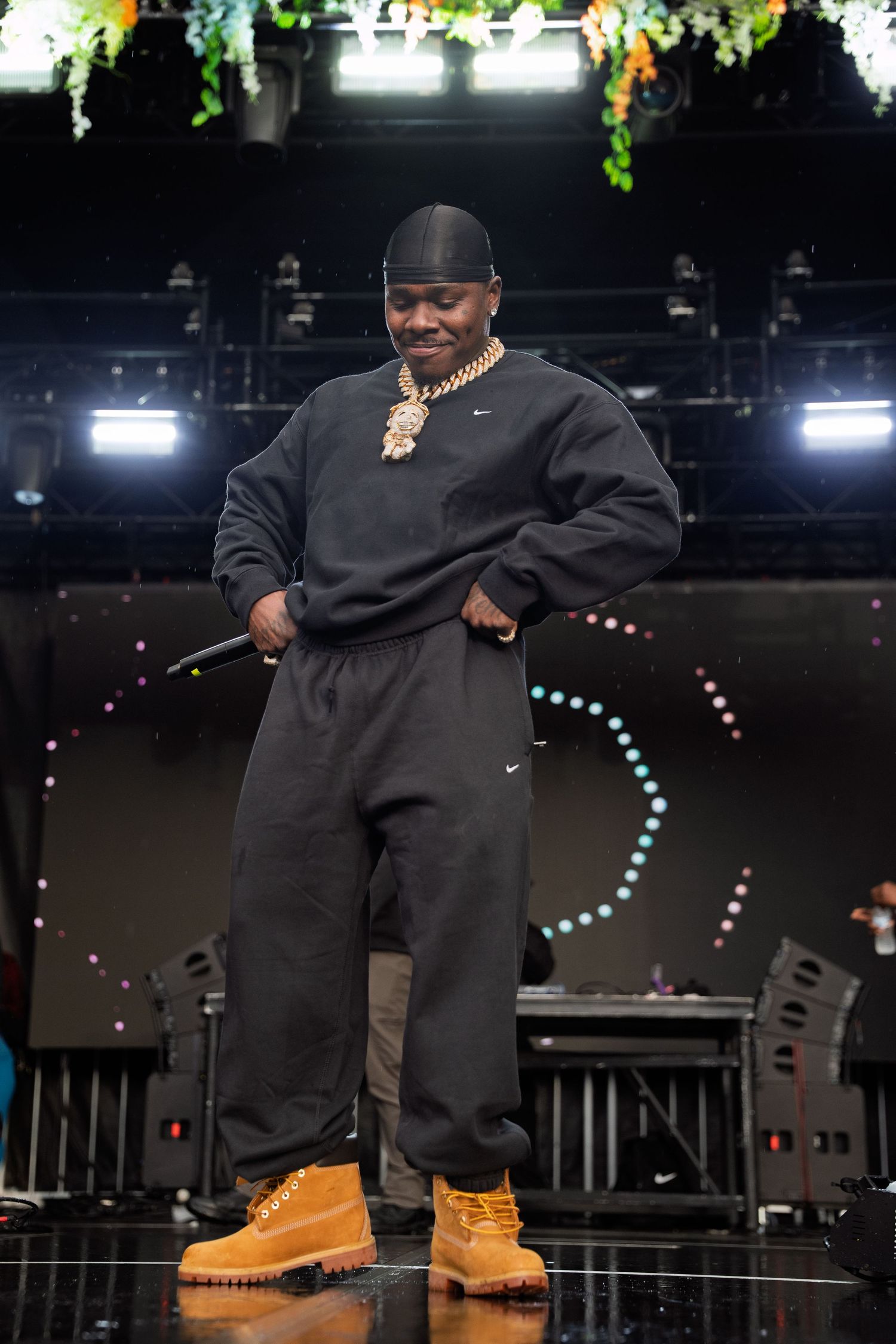 Performer in black Nike sweats and Timberland boots poses on stage with gold chain jewelry.