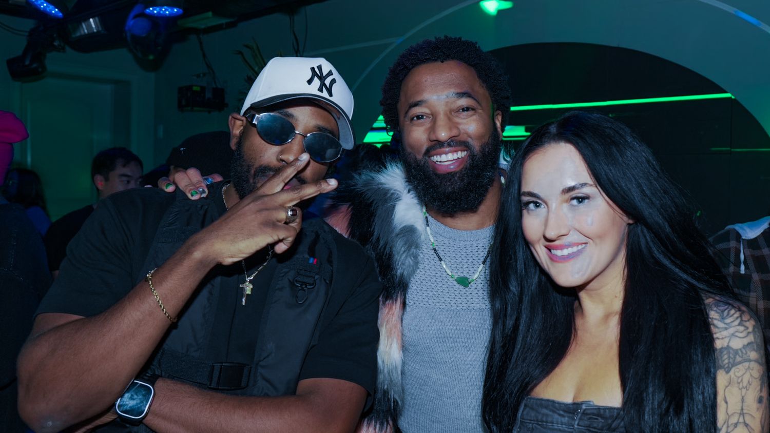 Three friends posing and smiling together at a vibrant nightclub event.