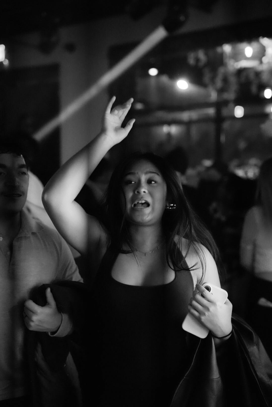 Black and white photo of a young woman dancing with her arm raised at a nightclub event.