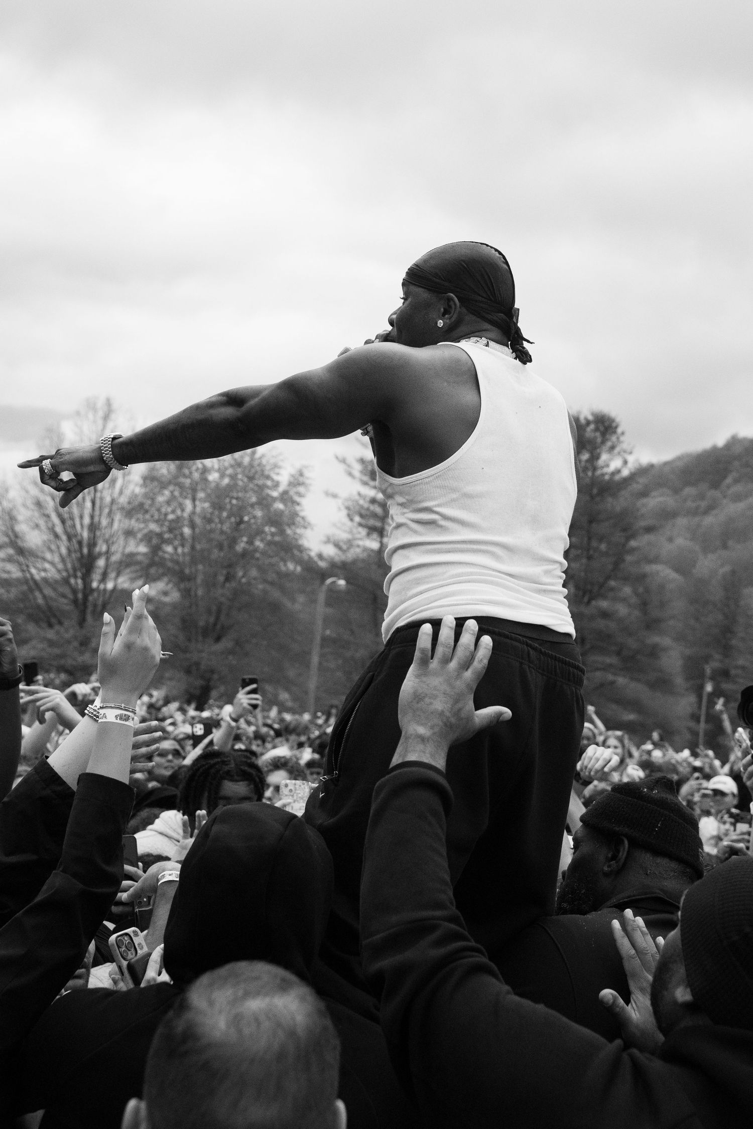 Black and white rear view of male performer pointing into massive outdoor festival crowd from elevated position.