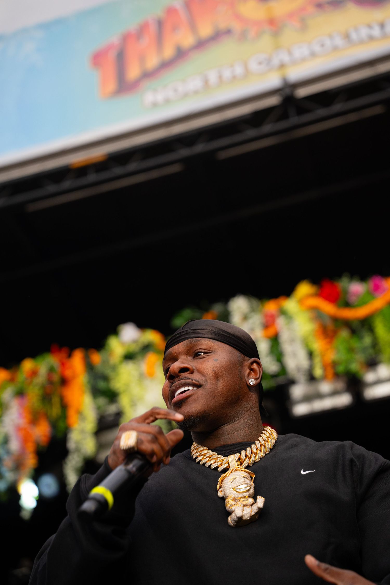 Close-up of rapper performing on outdoor stage wearing black Nike shirt and gold chain necklace.