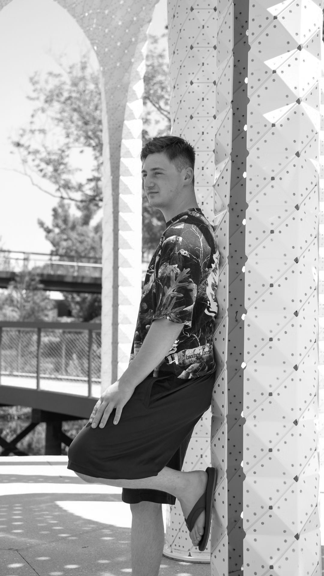 Black and white image of man leaning on art sculpture in park