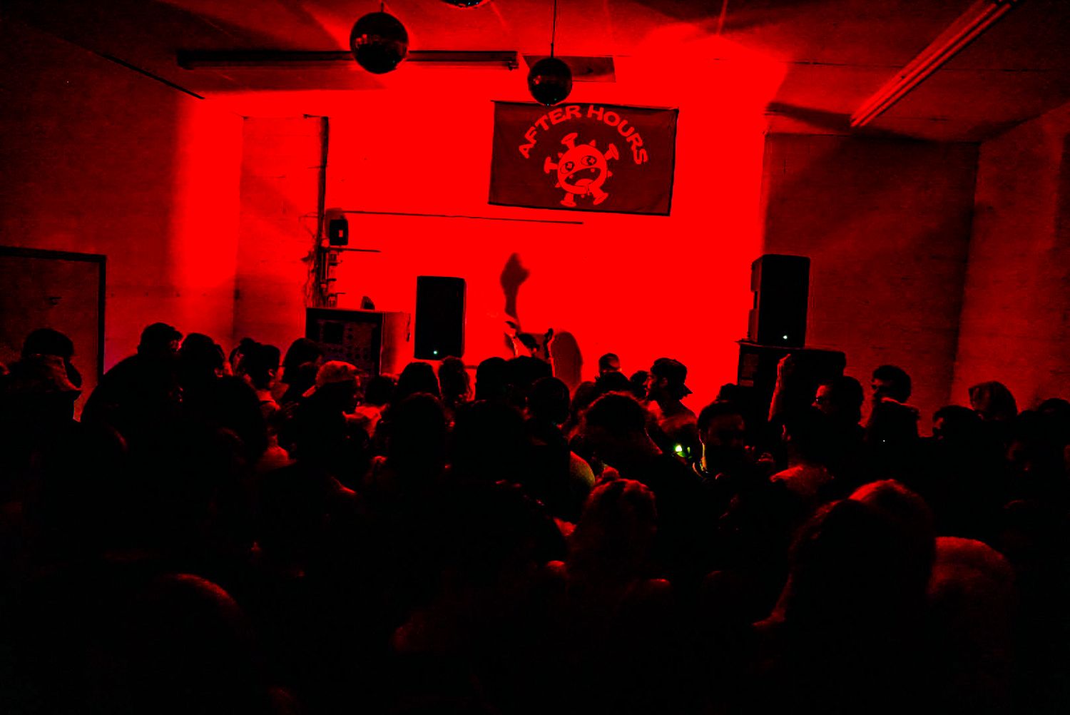 Silhouetted crowd at After Hours music event under intense red lighting.