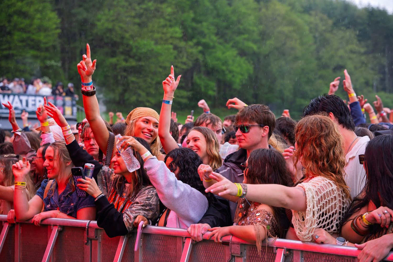Energetic concert crowd cheering with raised fists under red lights at an outdoor music festival.