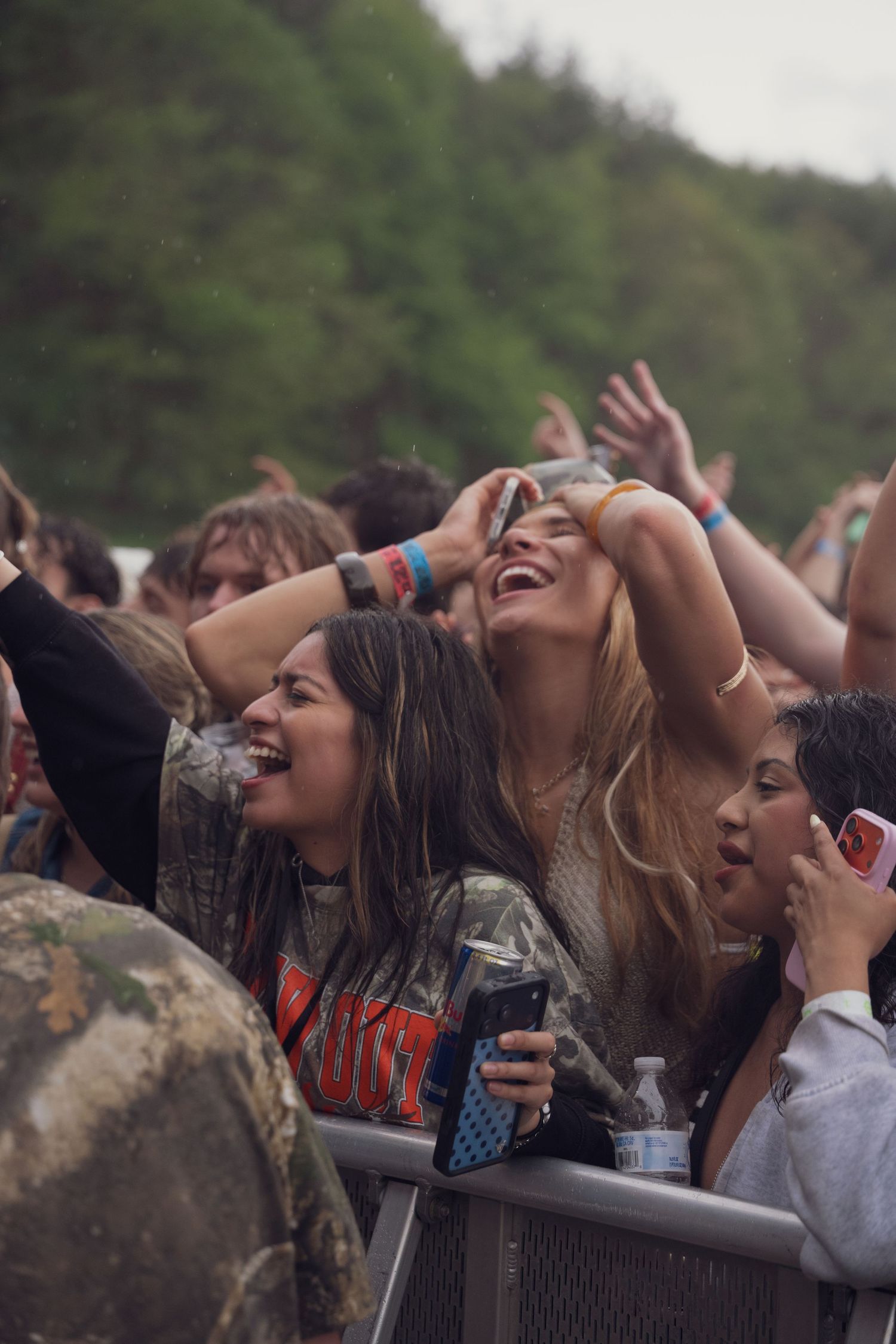 Excited female fans laughing and celebrating at outdoor music festival near crowd barrier.