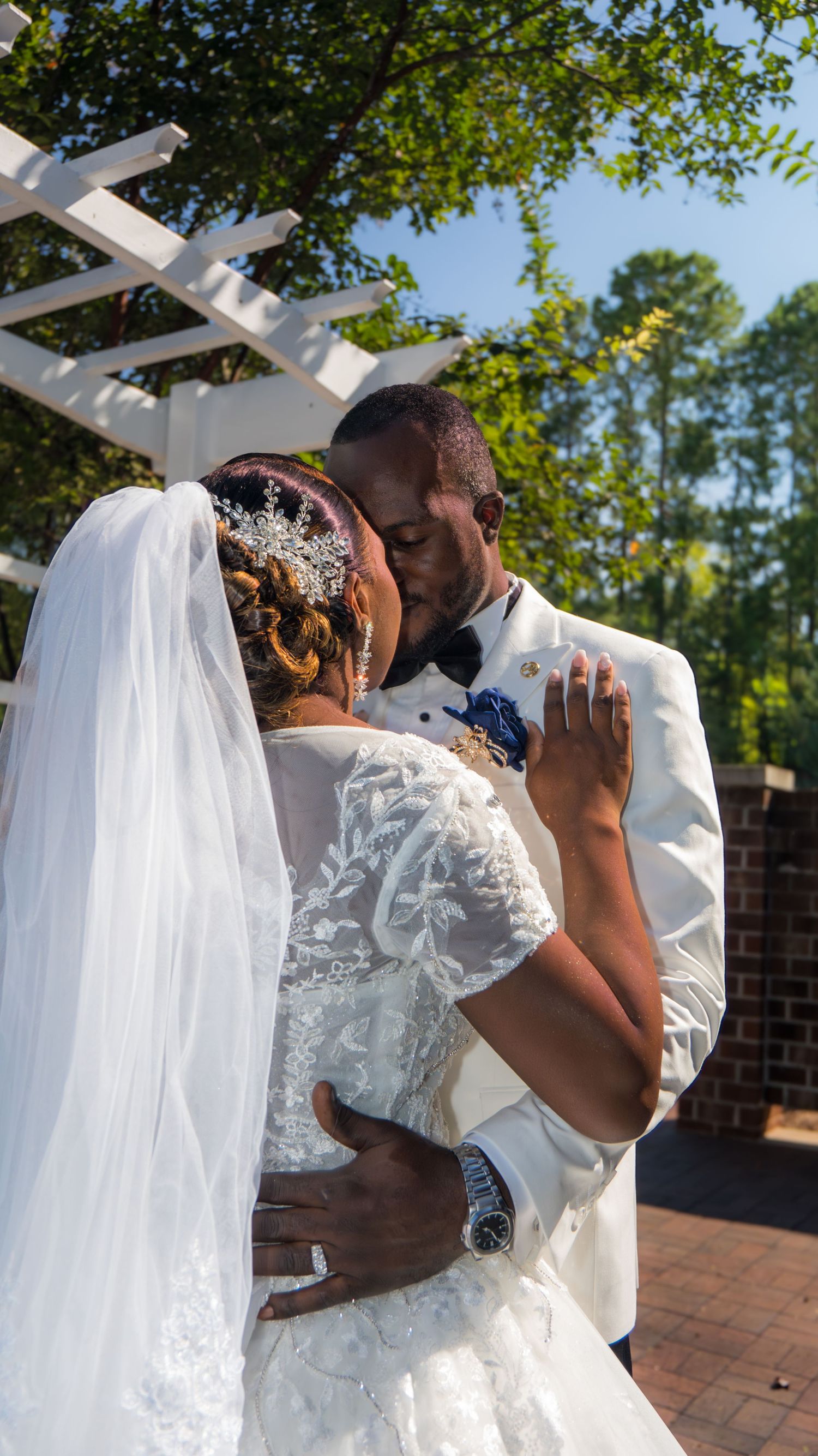 A bride and groom share a kiss under a white pergola at their outdoor wedding.