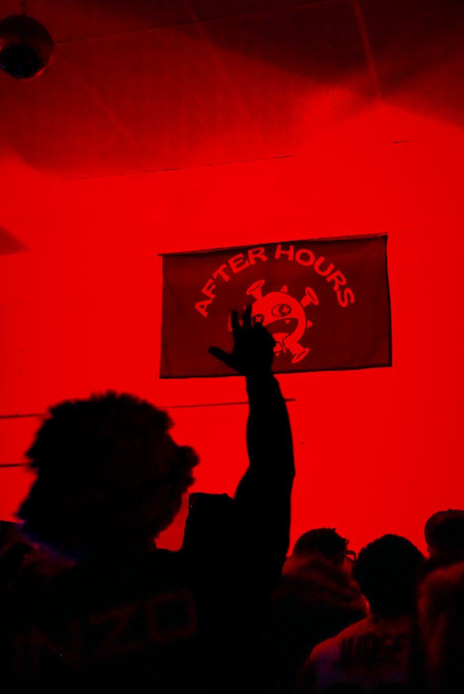 Silhouetted hand reaching toward After Hours banner in red-lit party venue.