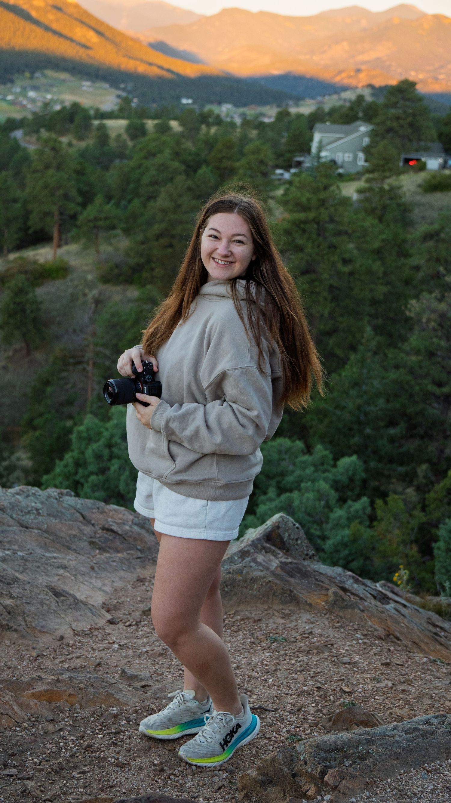 Woman standing on top of mountain with camera in hand and mountains in the background