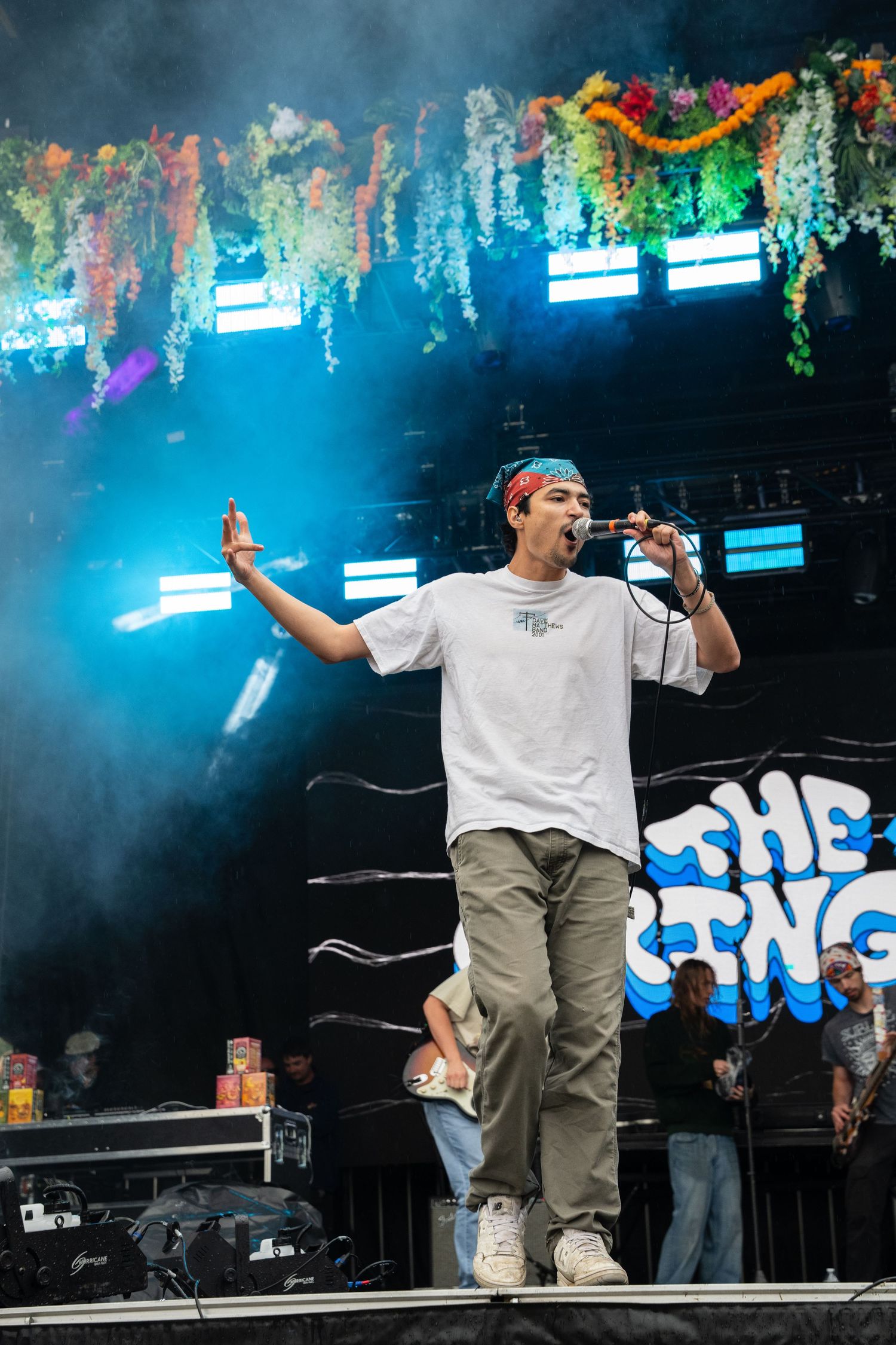 Male singer in red bandana performing on colorful floral decorated festival stage.