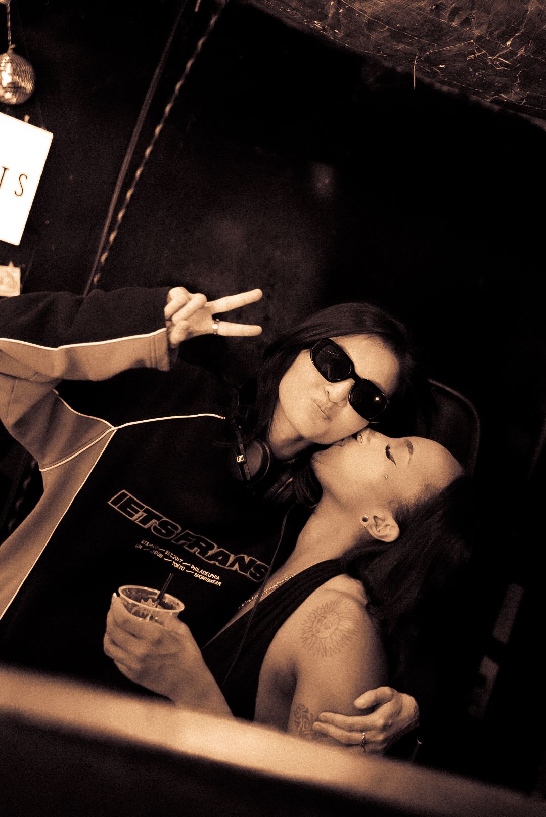 Two people sharing a kiss at a bar, one wearing a Jets Frans jacket.