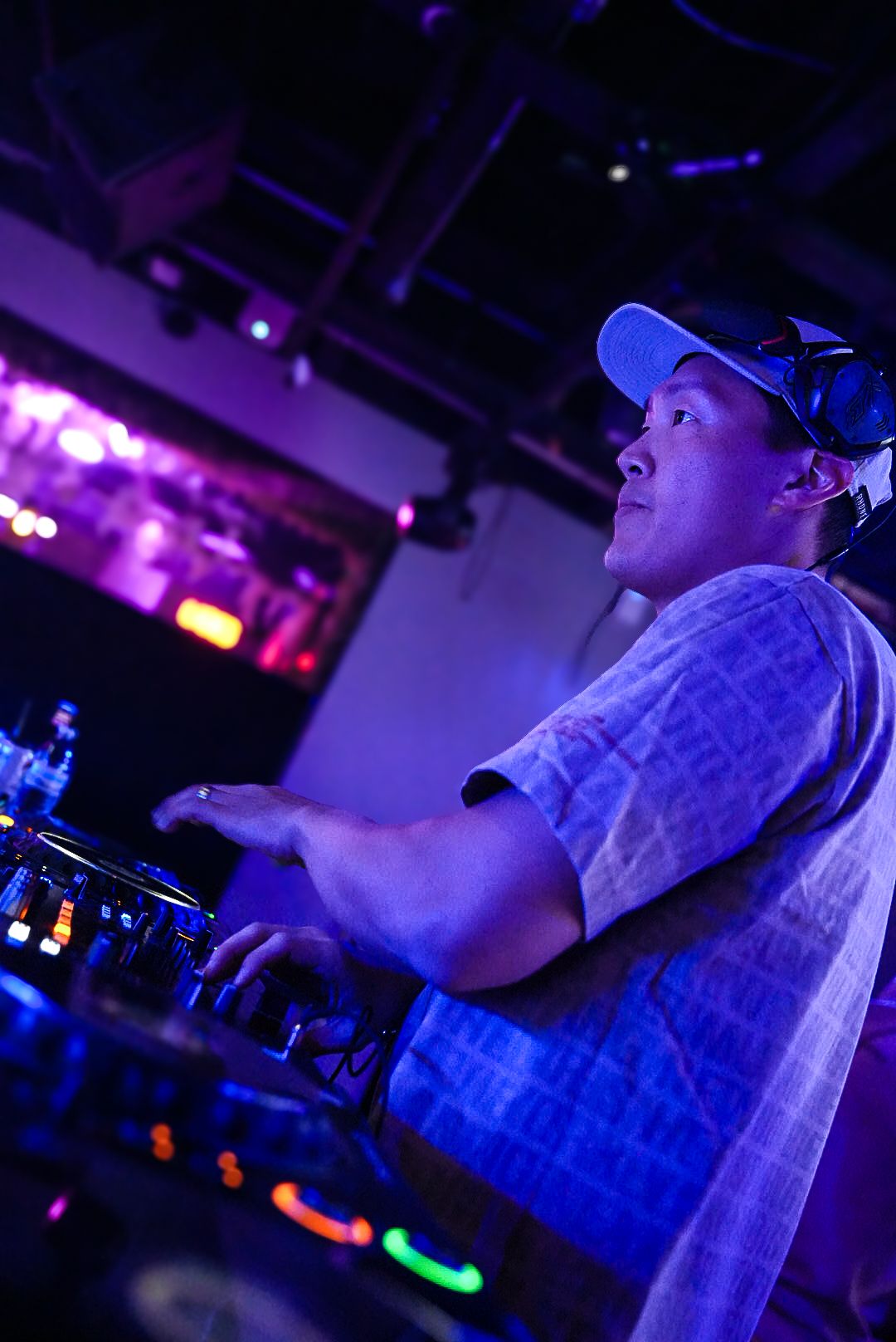 DJ in blue cap mixing tracks at turntables under purple nightclub lighting.