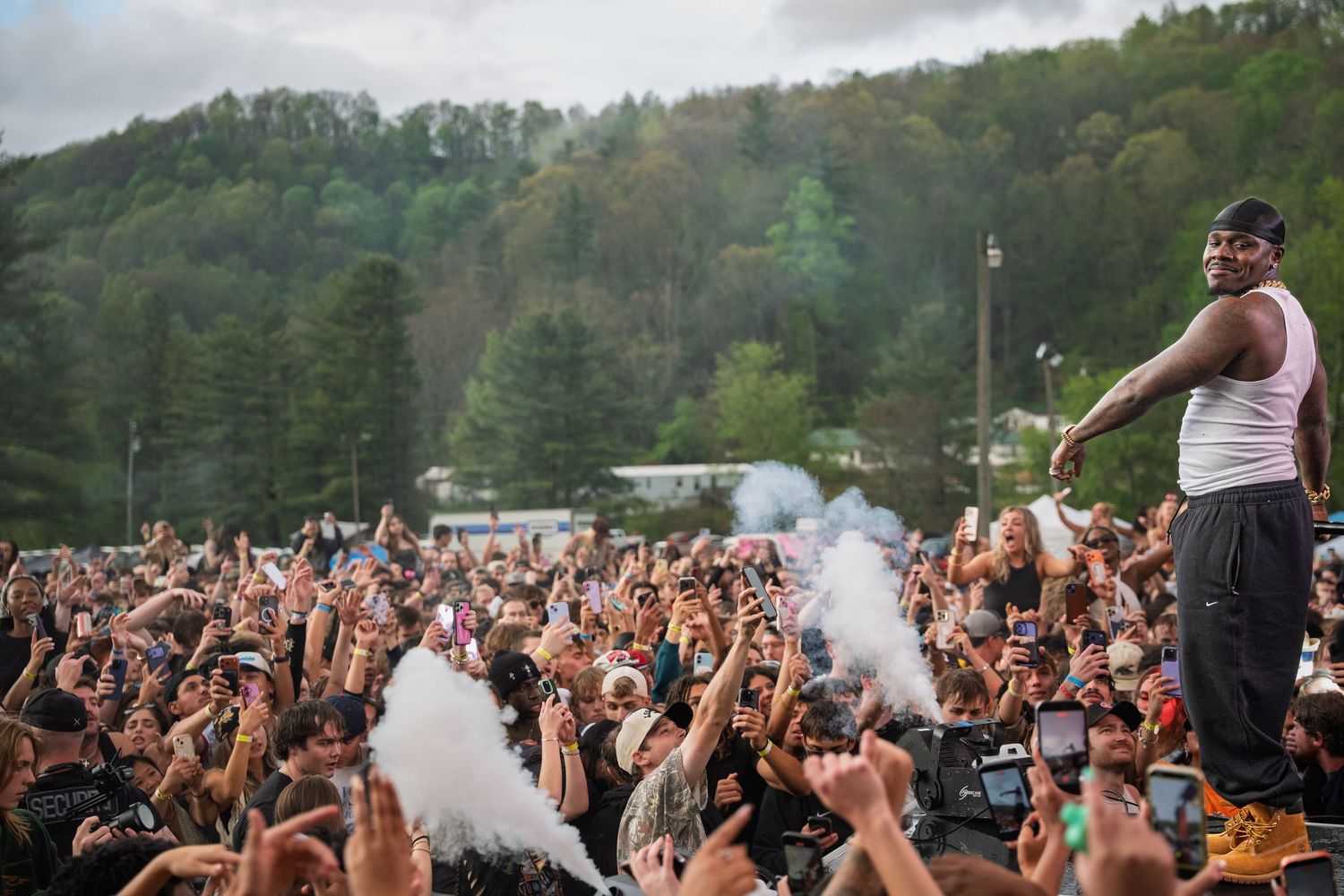 Performer stands elevated above large crowd with smoke effects at outdoor festival.