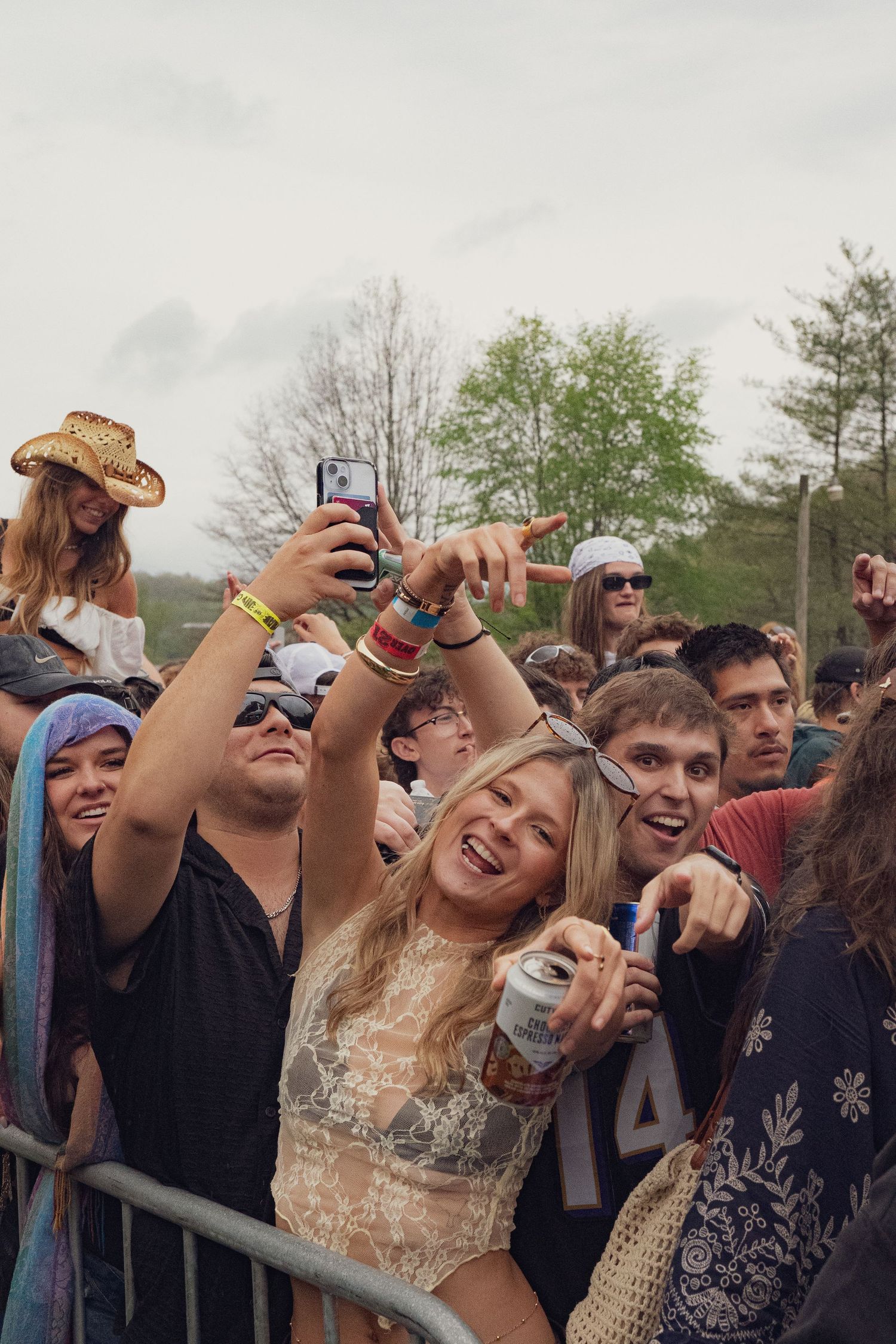 Smiling blonde woman holding beer can and phone in festive crowd at outdoor concert.