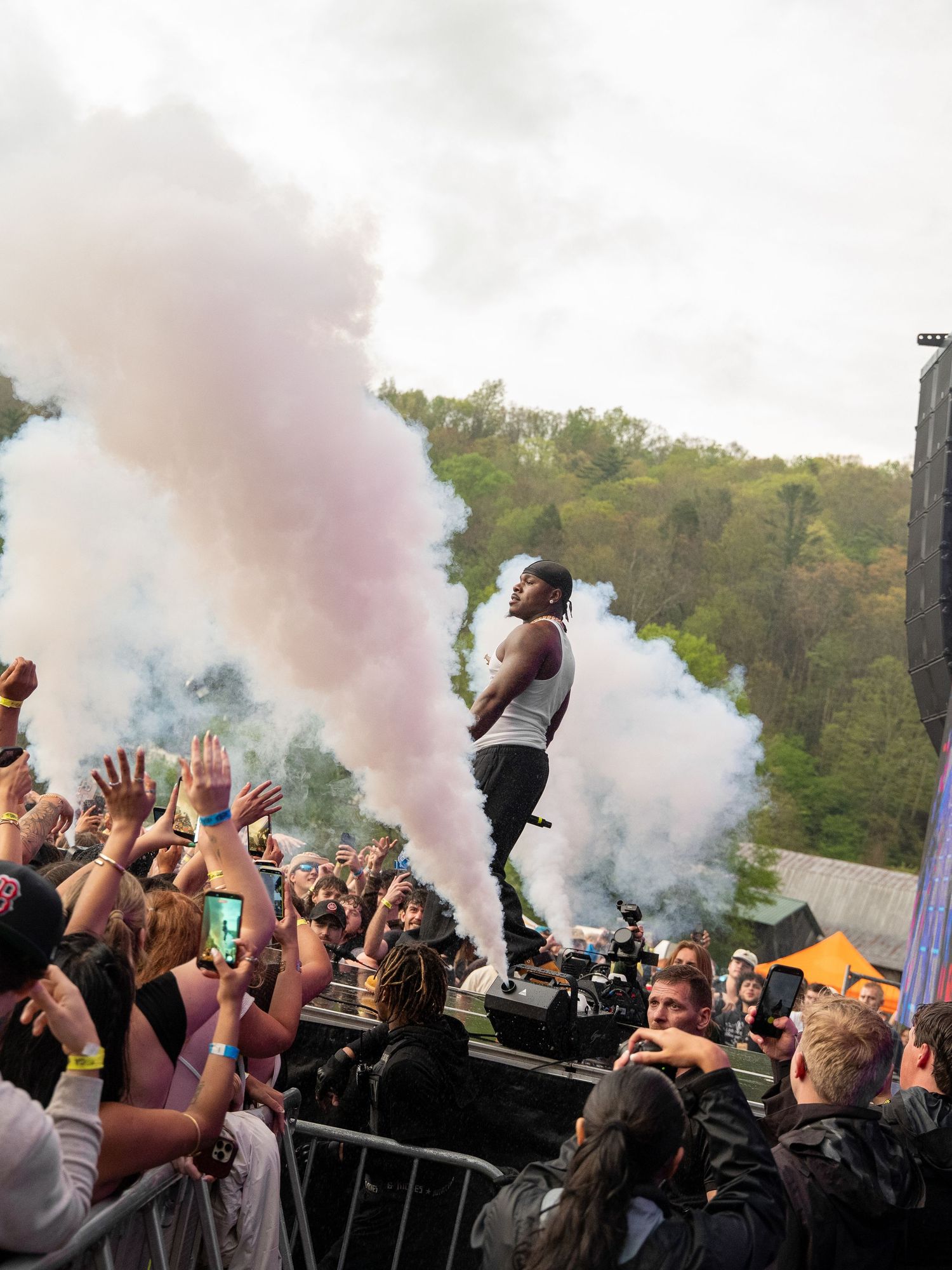 Rapper performs on elevated platform amid colorful smoke at outdoor music festival with crowd.
