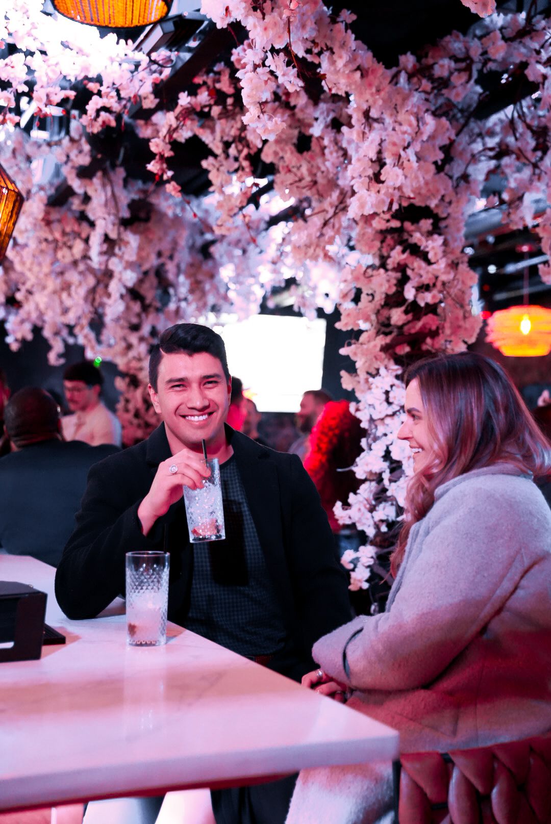 Couple enjoying drinks at a romantic restaurant decorated with pink cherry blossom flowers overhead.