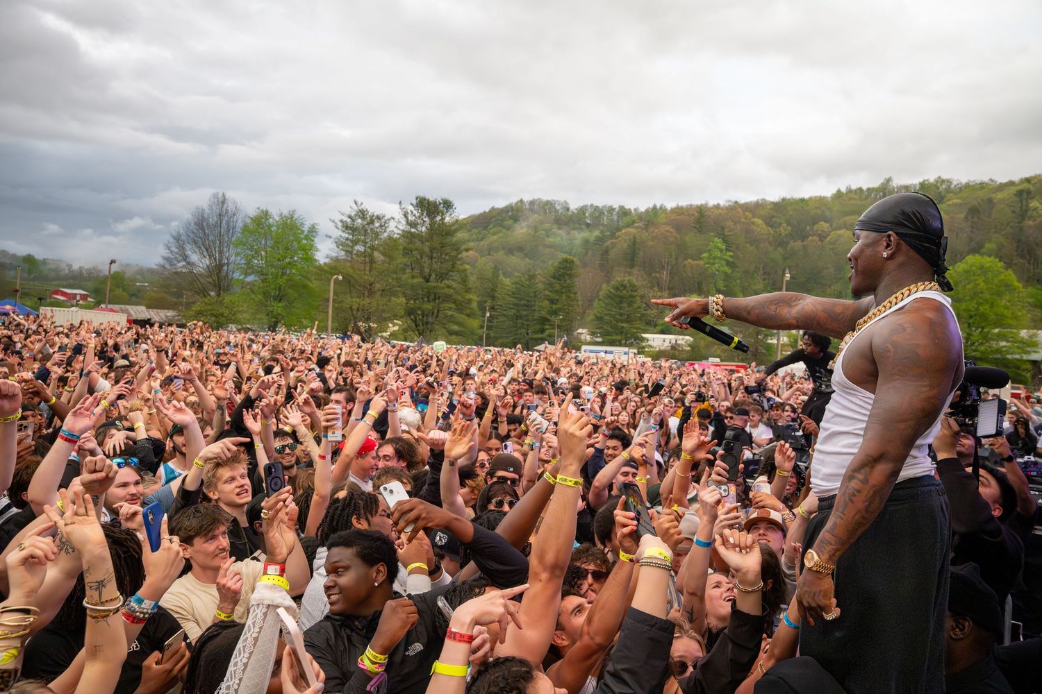 A shirtless rapper performs on stage before a massive outdoor festival crowd.