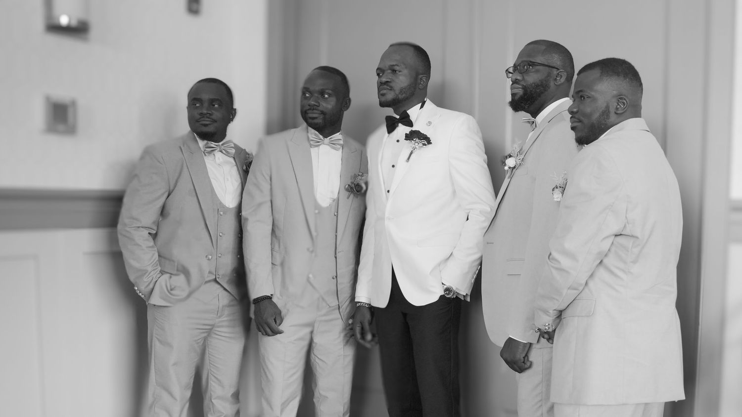 A groom and groomsmen in formal suits pose together in a black and white photo.