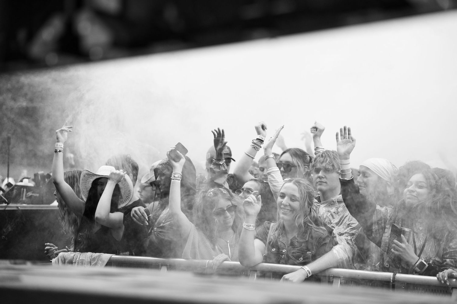 Black and white photo of joyful crowd with raised hands at an outdoor music festival stage.