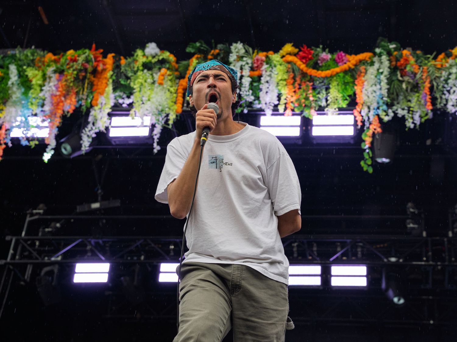 Male singer performing on stage with colorful floral decorations overhead.