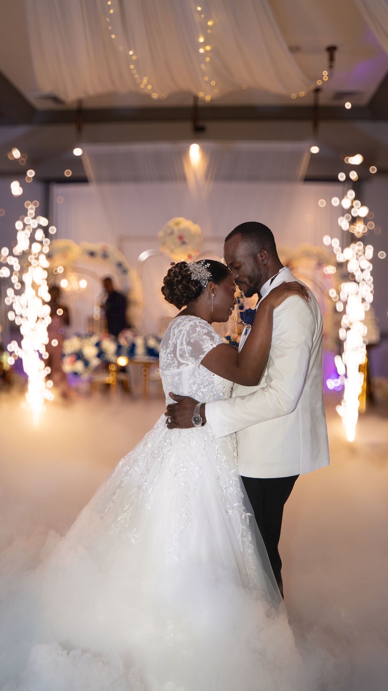 Bride and groom sharing first dance surrounded by sparkling lights and romantic fog-filled wedding reception.