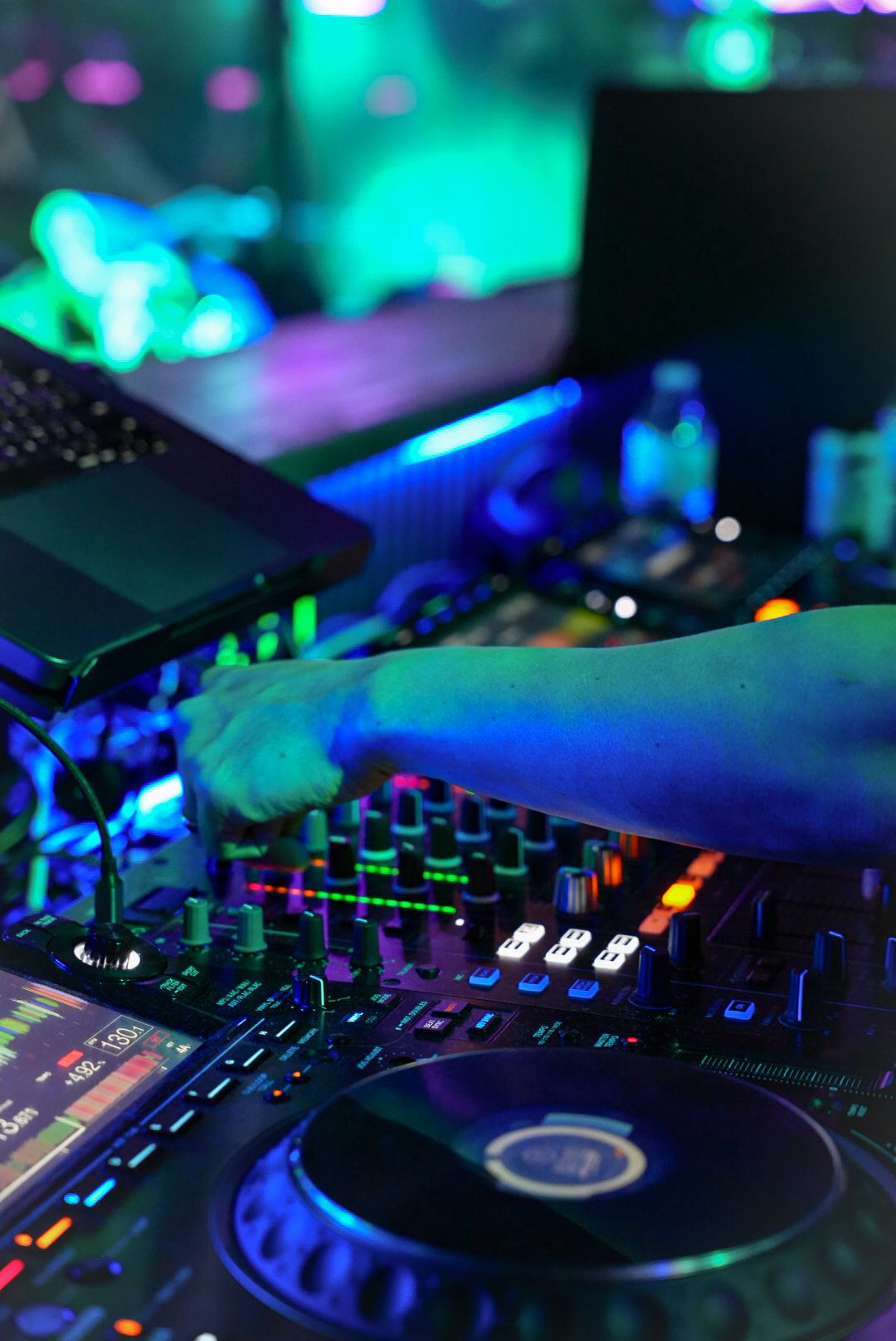 Close-up of DJ hands operating a professional Pioneer DJ mixer with colorful neon club lighting.