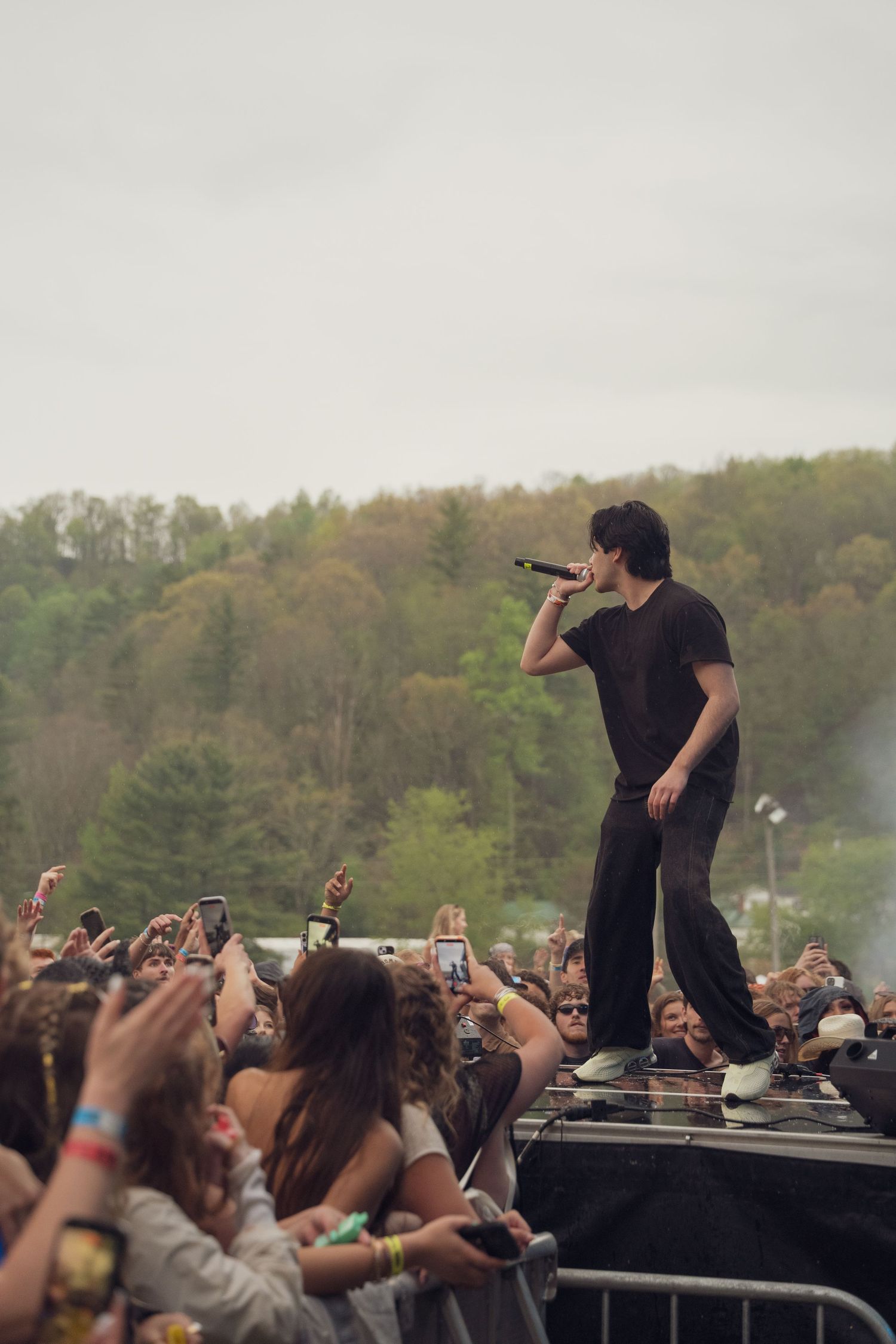 A male performer raps into a microphone while standing above the crowd at an outdoor festival.
