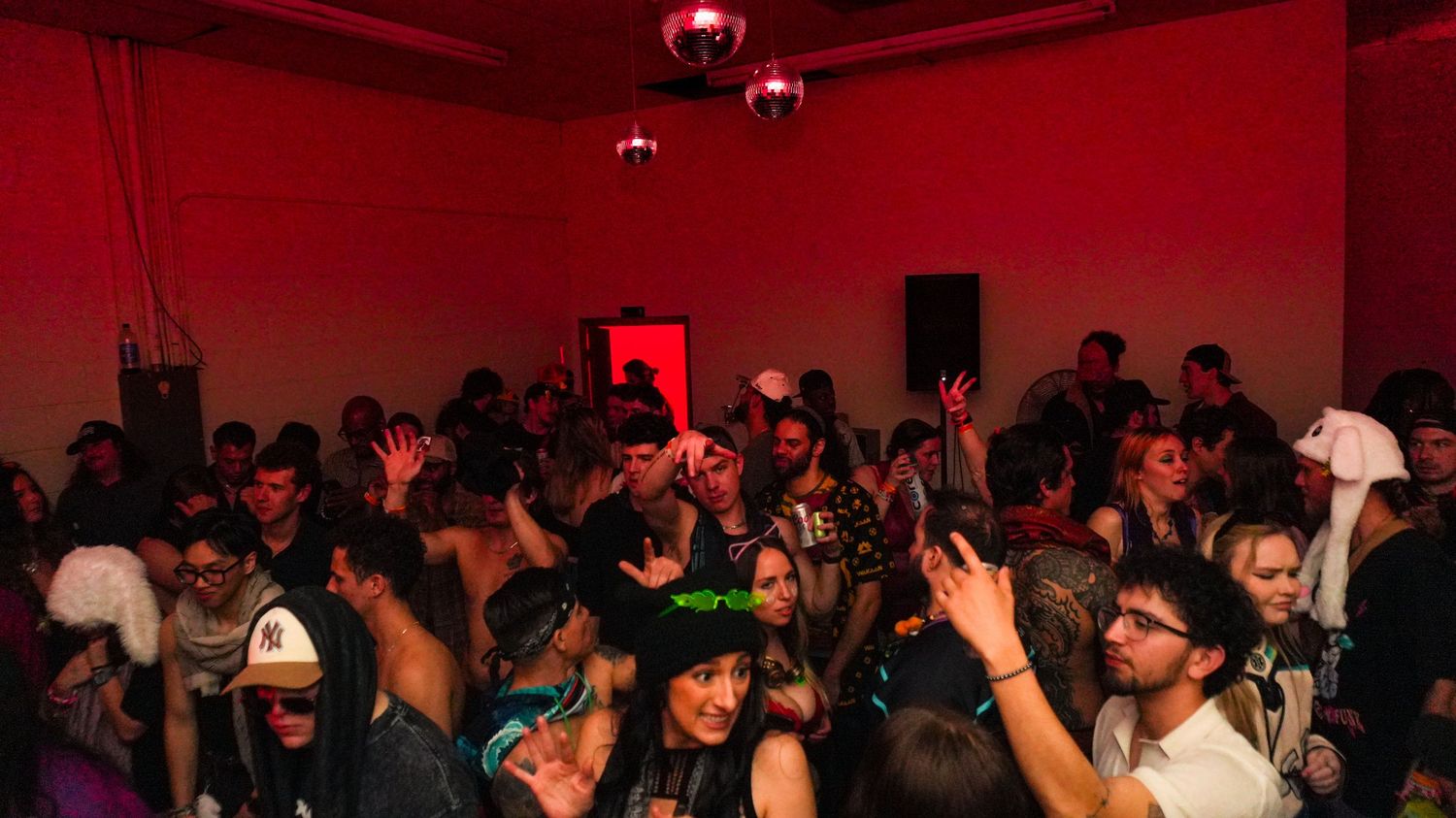 Large crowd dancing under red lights at an After Hours underground party.