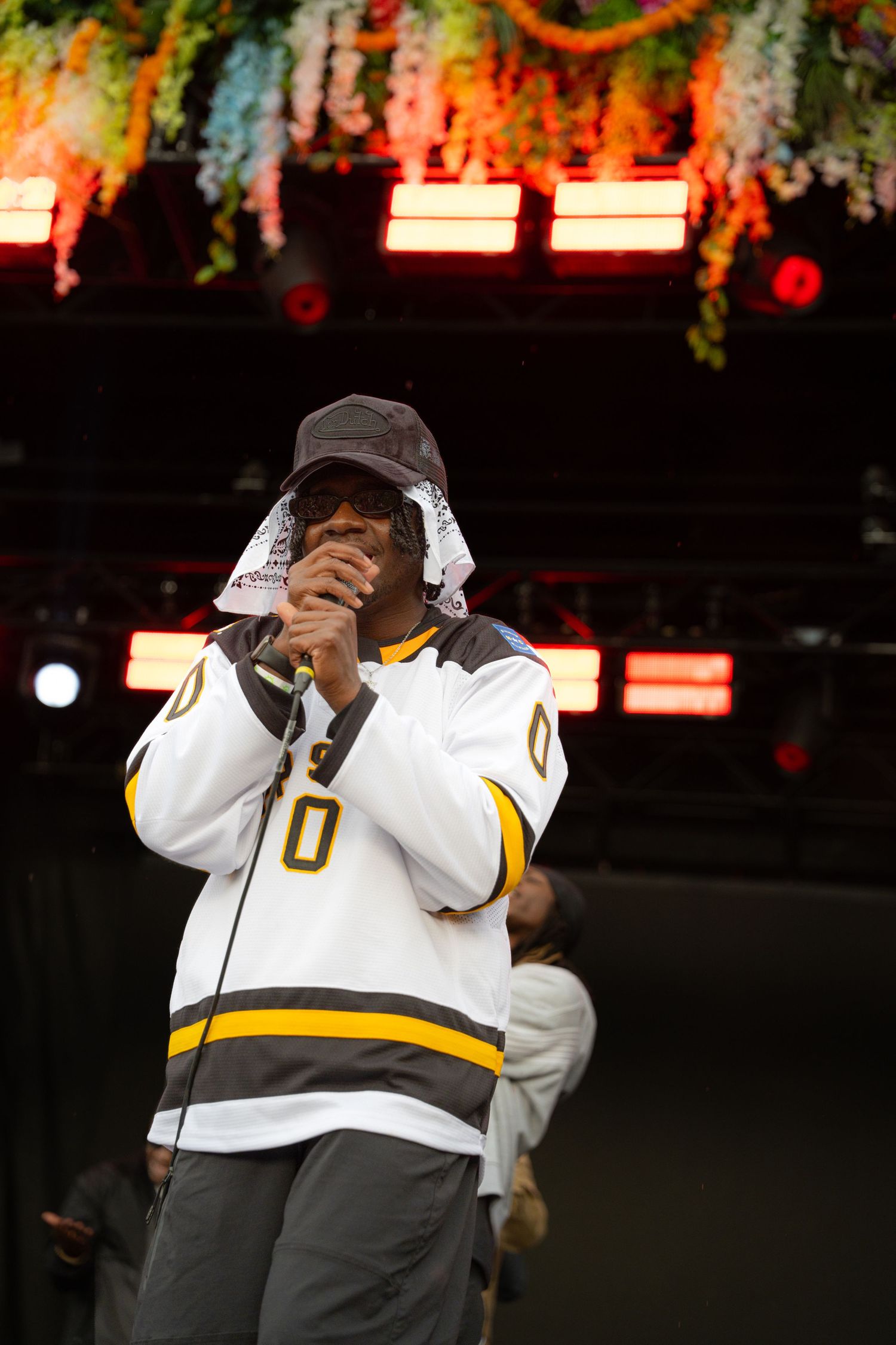 Rapper in App State number 0 jersey performs on stage with bandana over face.