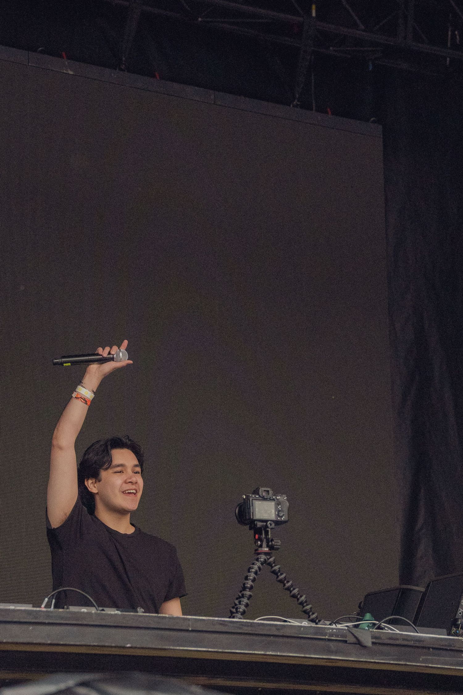 Young male performer holding microphone aloft on stage with camera on tripod nearby.