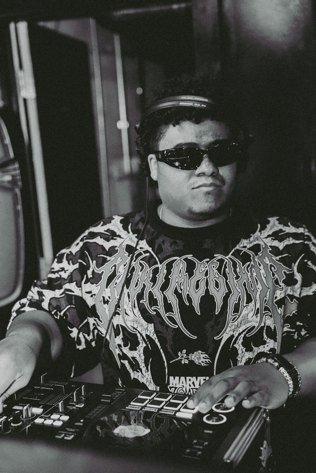 DJ in Thrasher shirt and sunglasses operating turntables in black and white photo.