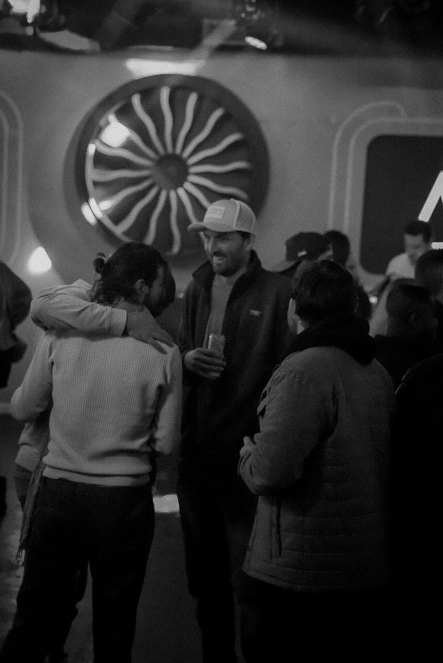Black and white photo of people socializing at a nightclub with a decorative wall art in the background.