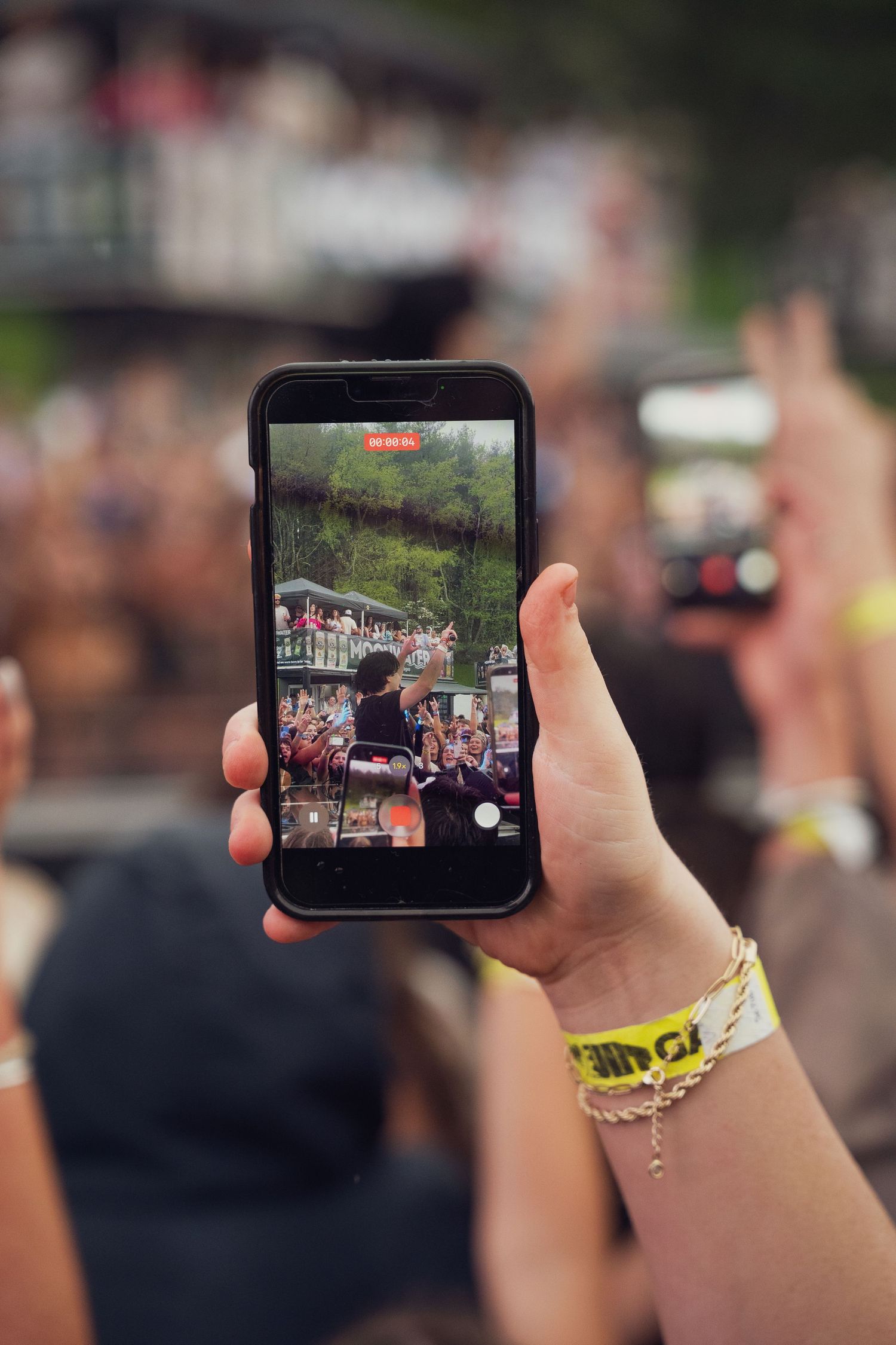 A hand holds up a smartphone recording a live outdoor music festival performance on screen.