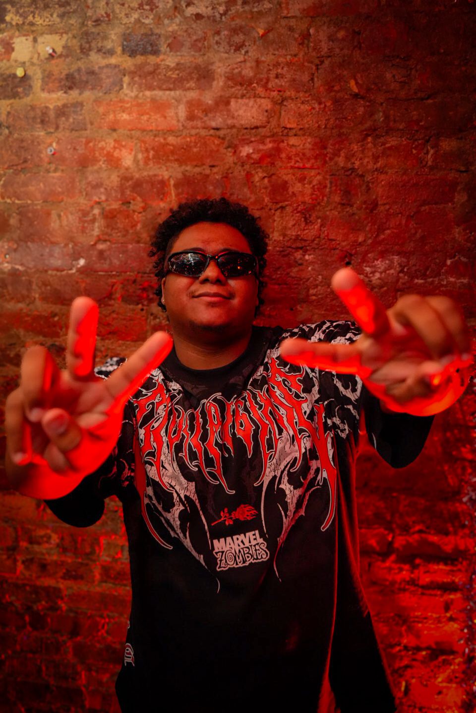 Young man in Marvel Zombies shirt making rock signs under red light.