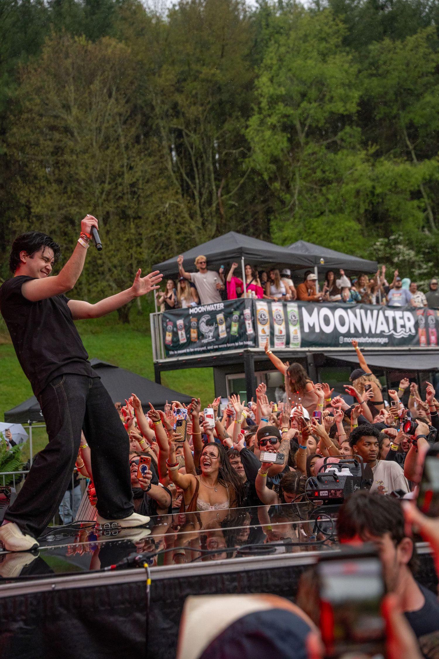 A musician in black performs on stage before a large cheering crowd at a Moonwater outdoor festival.