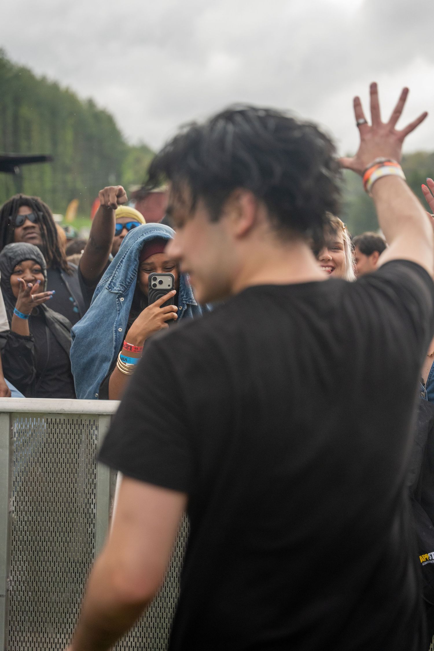 Performer in black t-shirt faces excited fans taking photos at outdoor music festival.