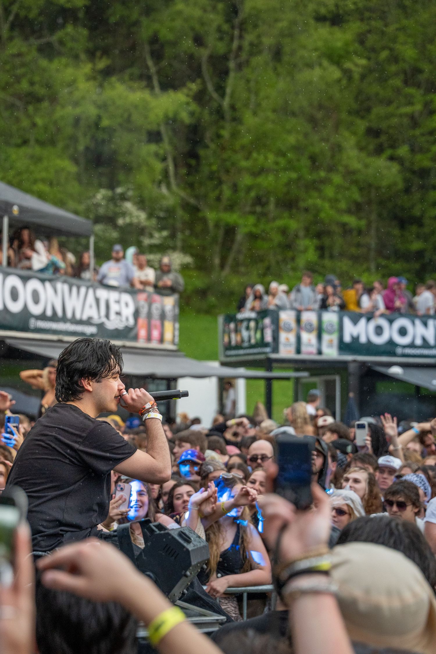 Performer singing into microphone on stage at Moonwater outdoor music festival with crowd below.
