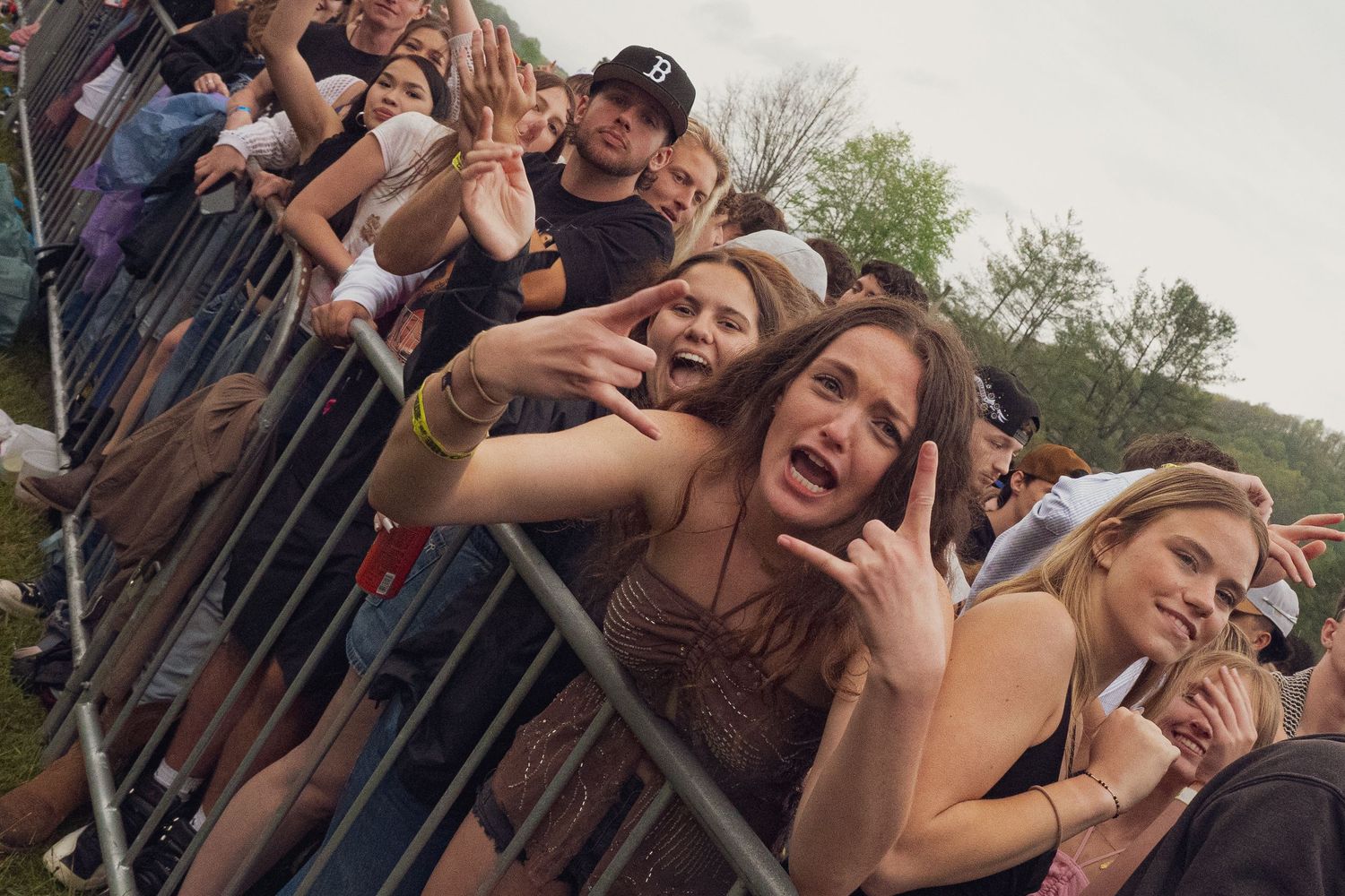 Excited young women making rock signs at metal barrier at outdoor music festival.