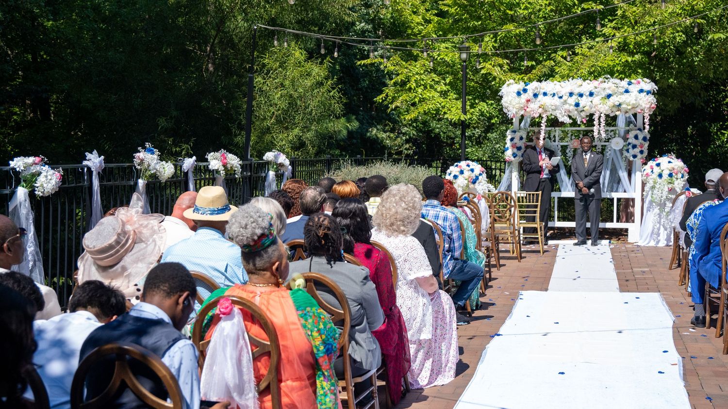 Guests seated along a white aisle watch a couple at an elegant outdoor wedding ceremony.