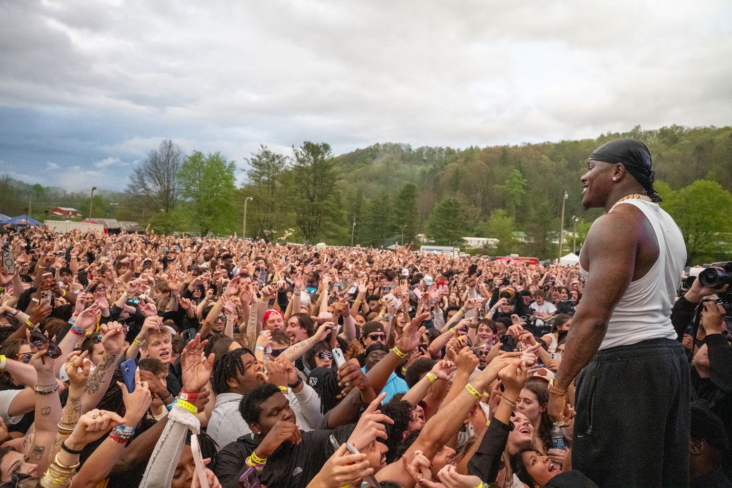 A rapper engages an energetic crowd at a large outdoor music festival event.