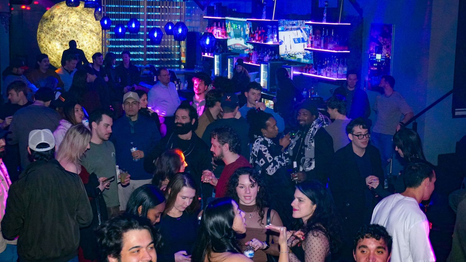 Diverse crowd socializing and dancing inside a dimly lit nightclub venue.