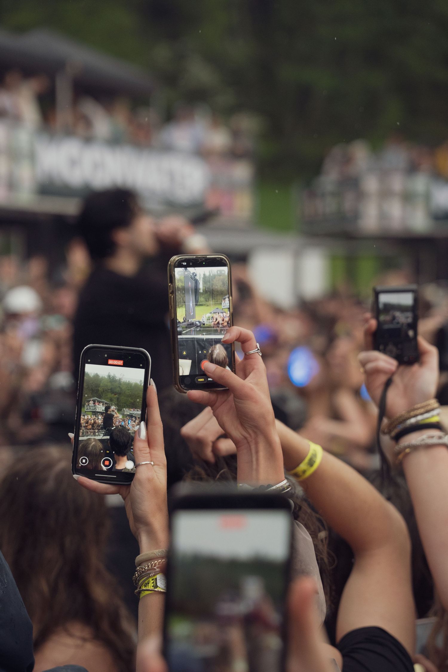 Concert fans hold up smartphones to record a live outdoor music festival performance.