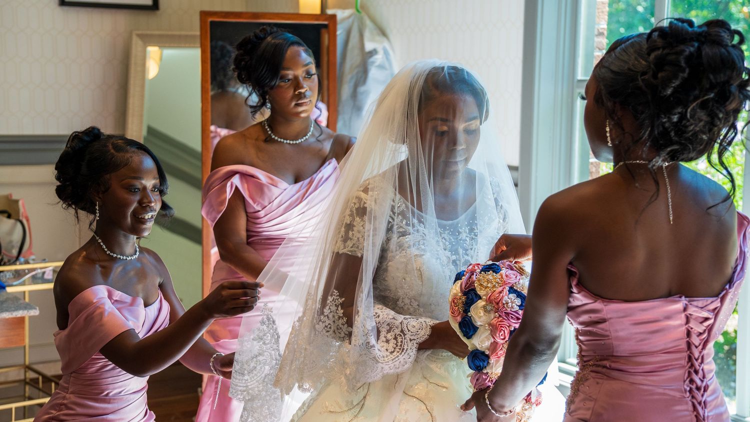 Bridesmaids in pink dresses helping bride with veil and bouquet before wedding.