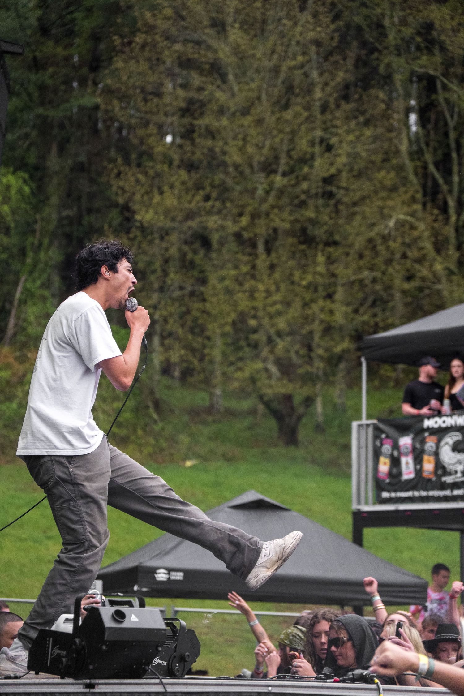 Male vocalist performing on stage edge, leaning toward crowd at outdoor music festival.