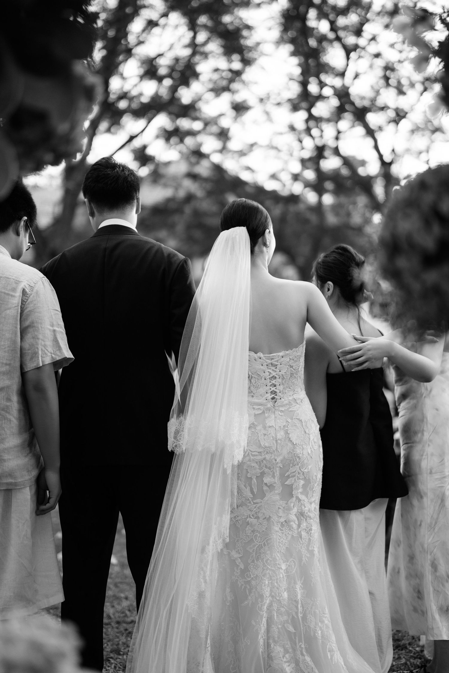 A black and white wedding photo series showing the back details of a lace bridal gown and veil.