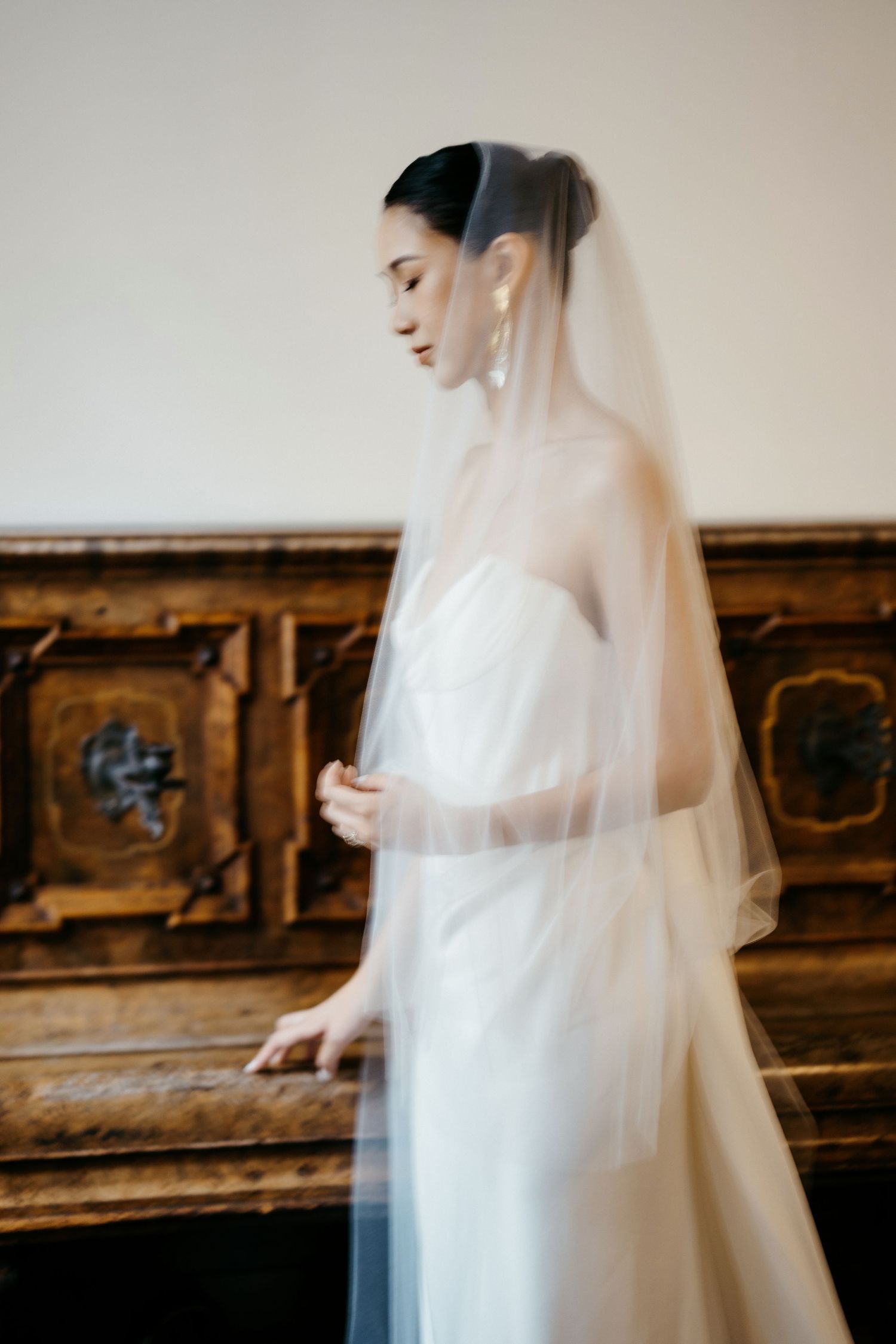 Ethereal bridal portrait with sheer veil against vintage wooden backdrop.