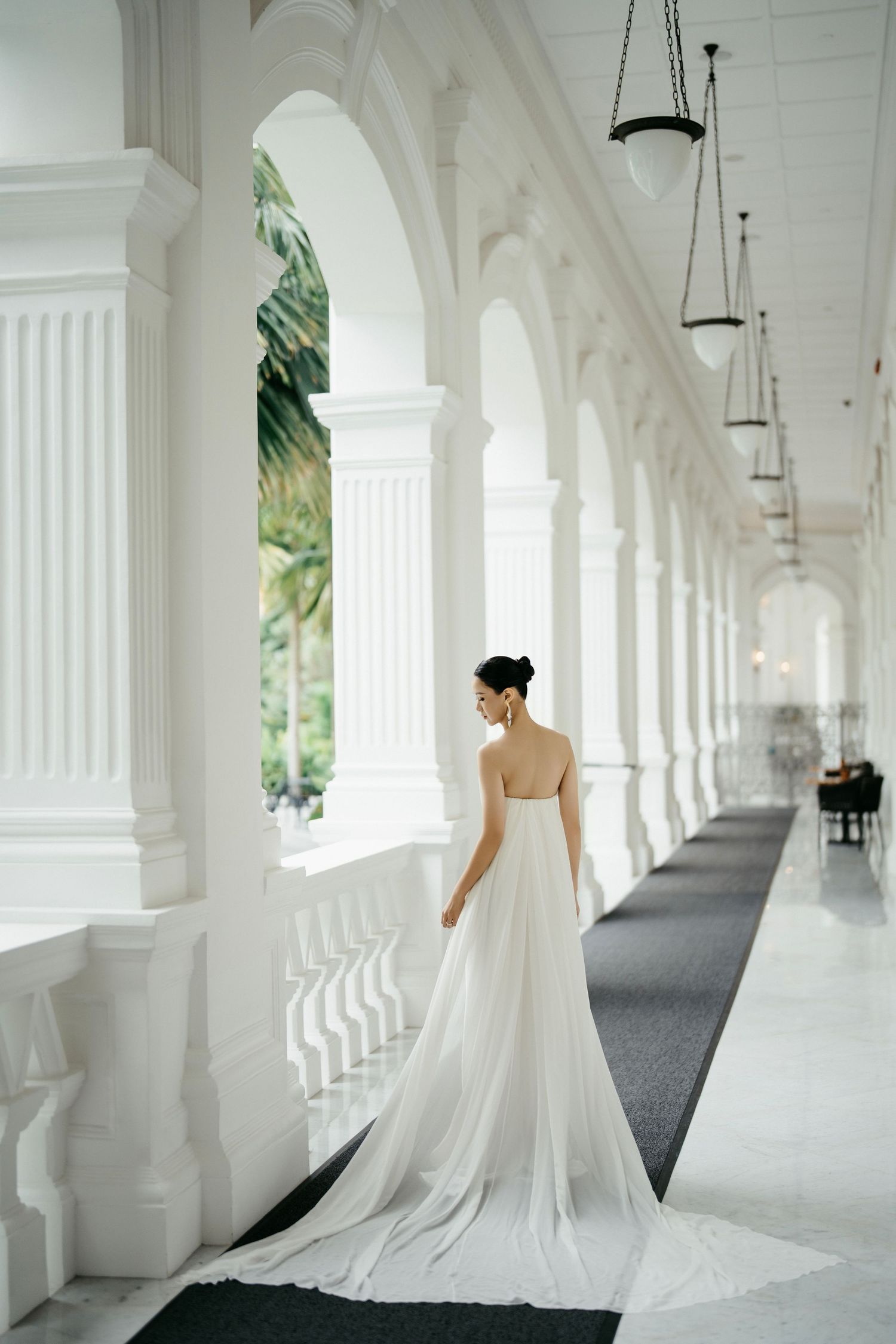Bride in flowing white gown walking along a colonial-style colonnade with hanging lanterns.
