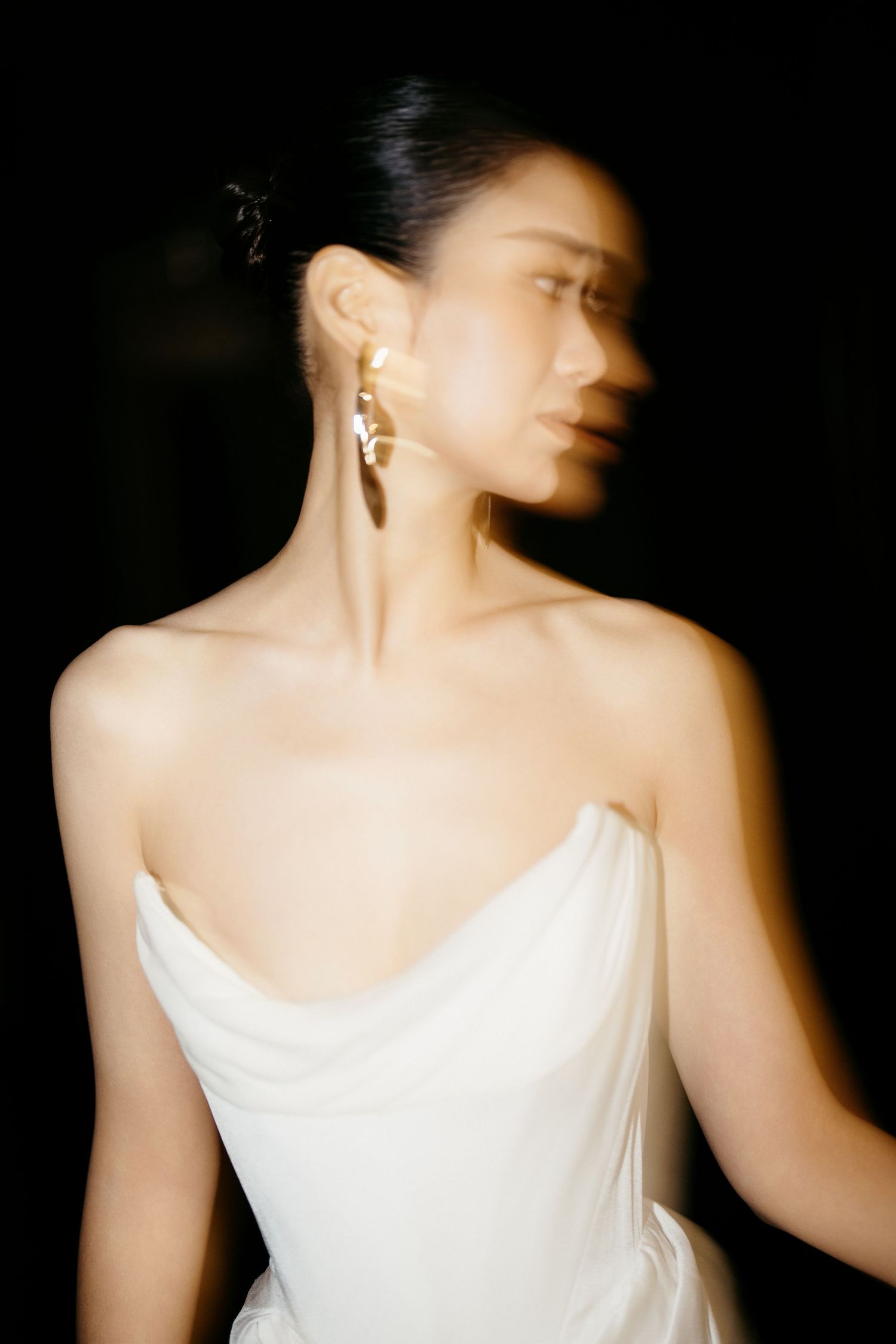 Artistic black and white portrait showcasing an elegant strapless wedding gown and statement earrings.