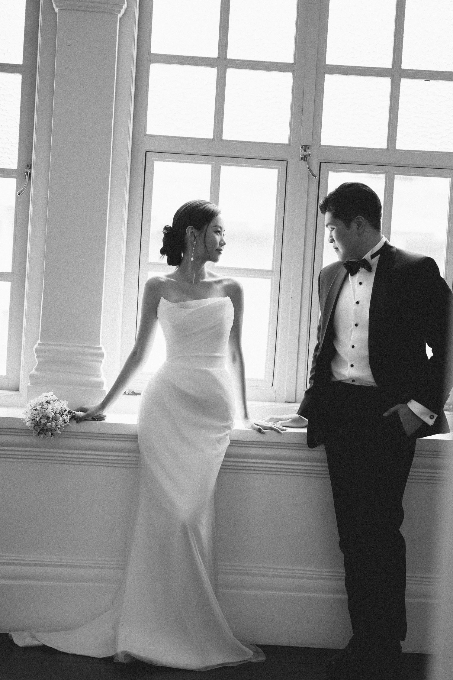 Wedding couple posing by bright windows in black and white photography sequence.