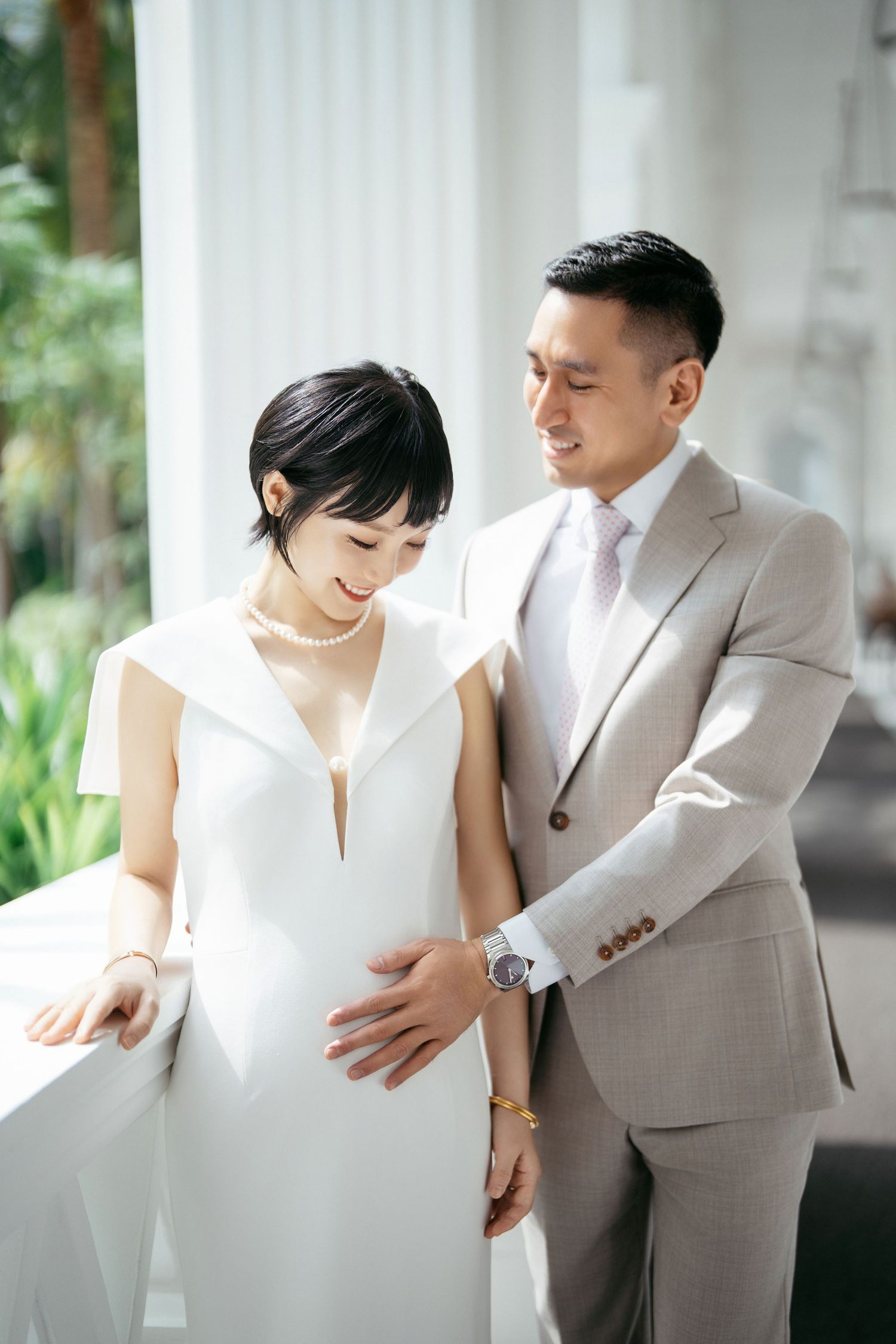 Couple in white dress and beige suit sharing intimate moment in outdoor setting.