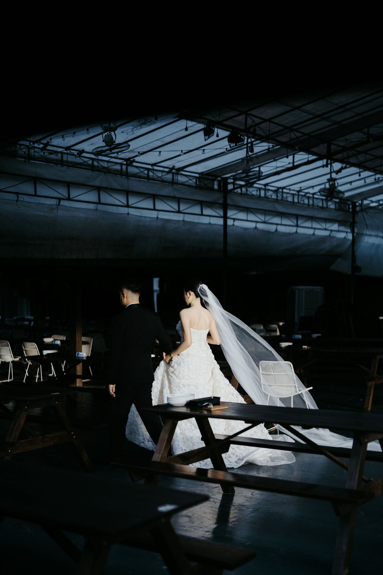 Dramatic silhouette of couple in wedding attire under industrial ceiling with dramatic lighting.